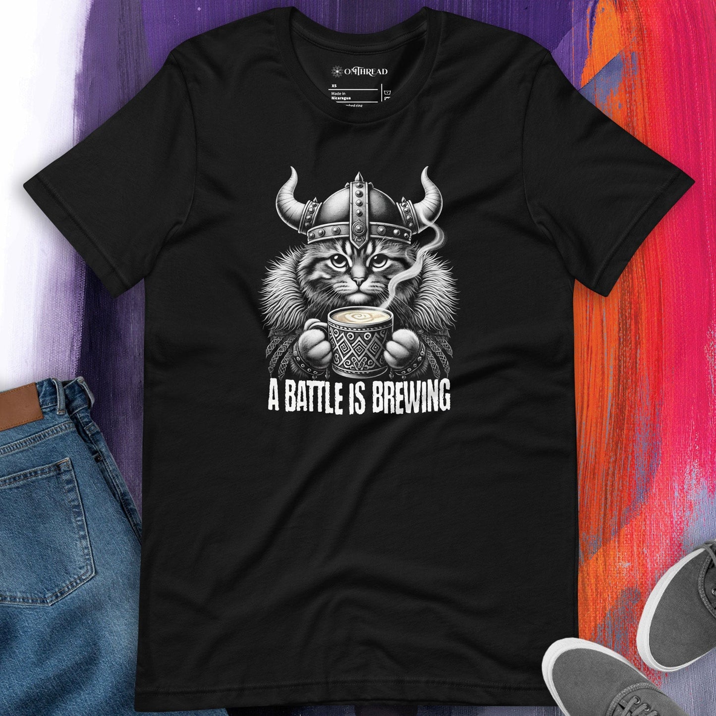 OMTHREAD A Battle Is Brewing Viking Cat Black T-Shirt featuring a fierce feline in Norse warrior gear holding a steaming cup of coffee. Perfect for coffee lovers, cat enthusiasts, and Viking mythology fans. Soft cotton unisex tee.