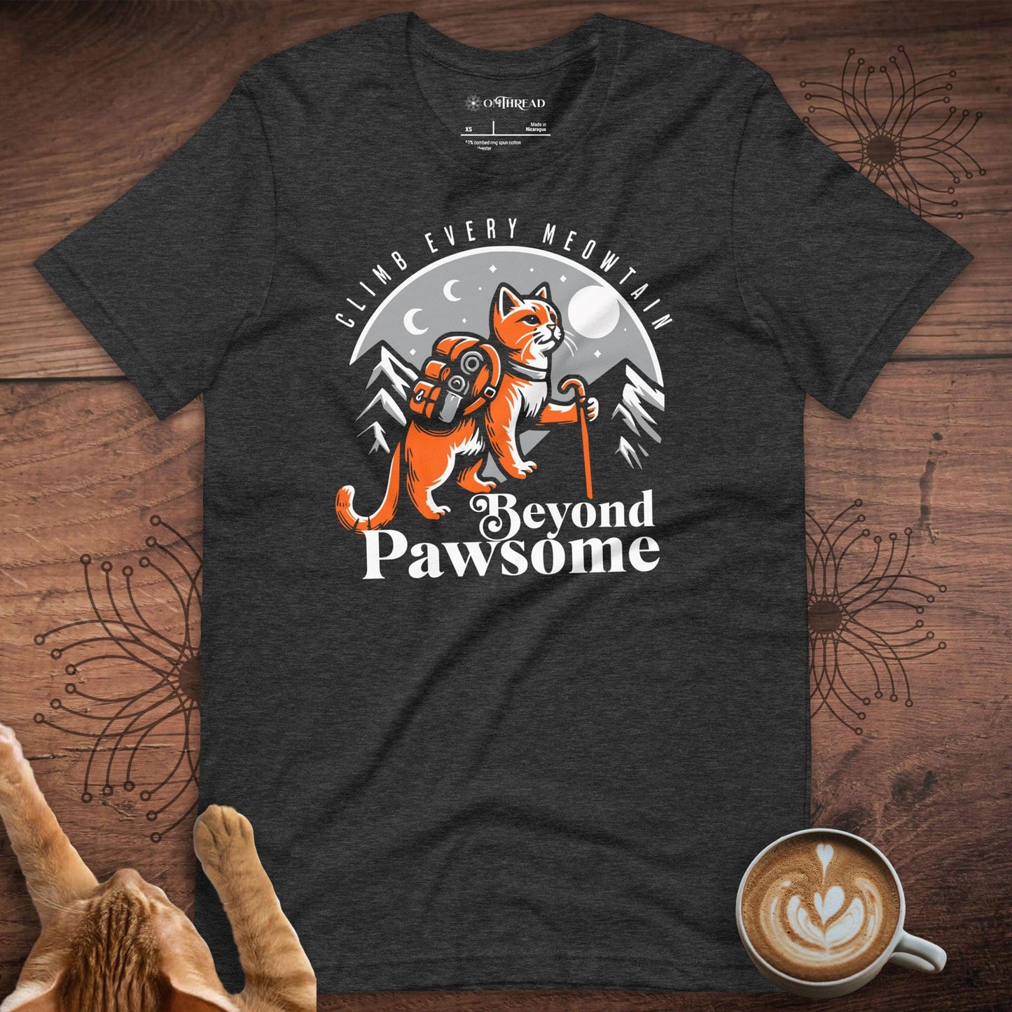 OMThread dark gray t-shirt featuring an adventurous orange cat with a backpack and hiking stick. The cat stands against a mountain and moonlit night backdrop. The design includes the text "Climb Every Meowntain" above and "Beyond Pawsome" below.