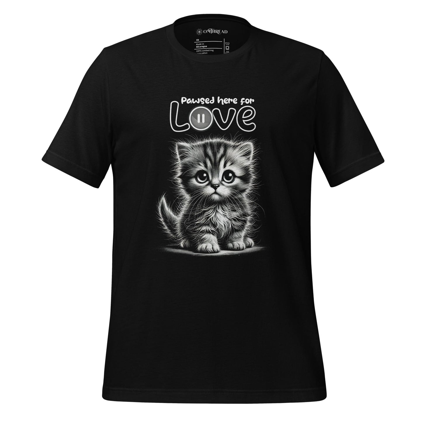 OMThread black t-shirt featuring a black and white illustration of a fluffy kitten with large expressive eyes. Above the kitten, the phrase "Pawsed Here for Love" is written in a playful font, with the word "Love" incorporating a pause button symbol.