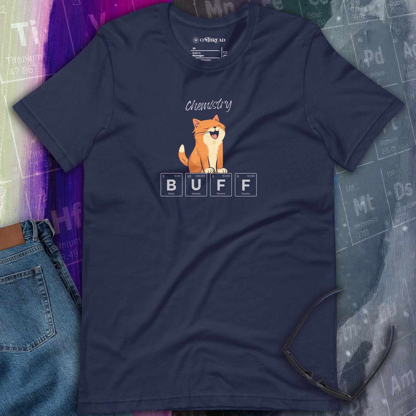 OMThread navy t-shirt featuring an orange cat flexing its muscles above periodic table elements spelling "BUFF." The design combines science and humor, with the word "Chemistry" written above.