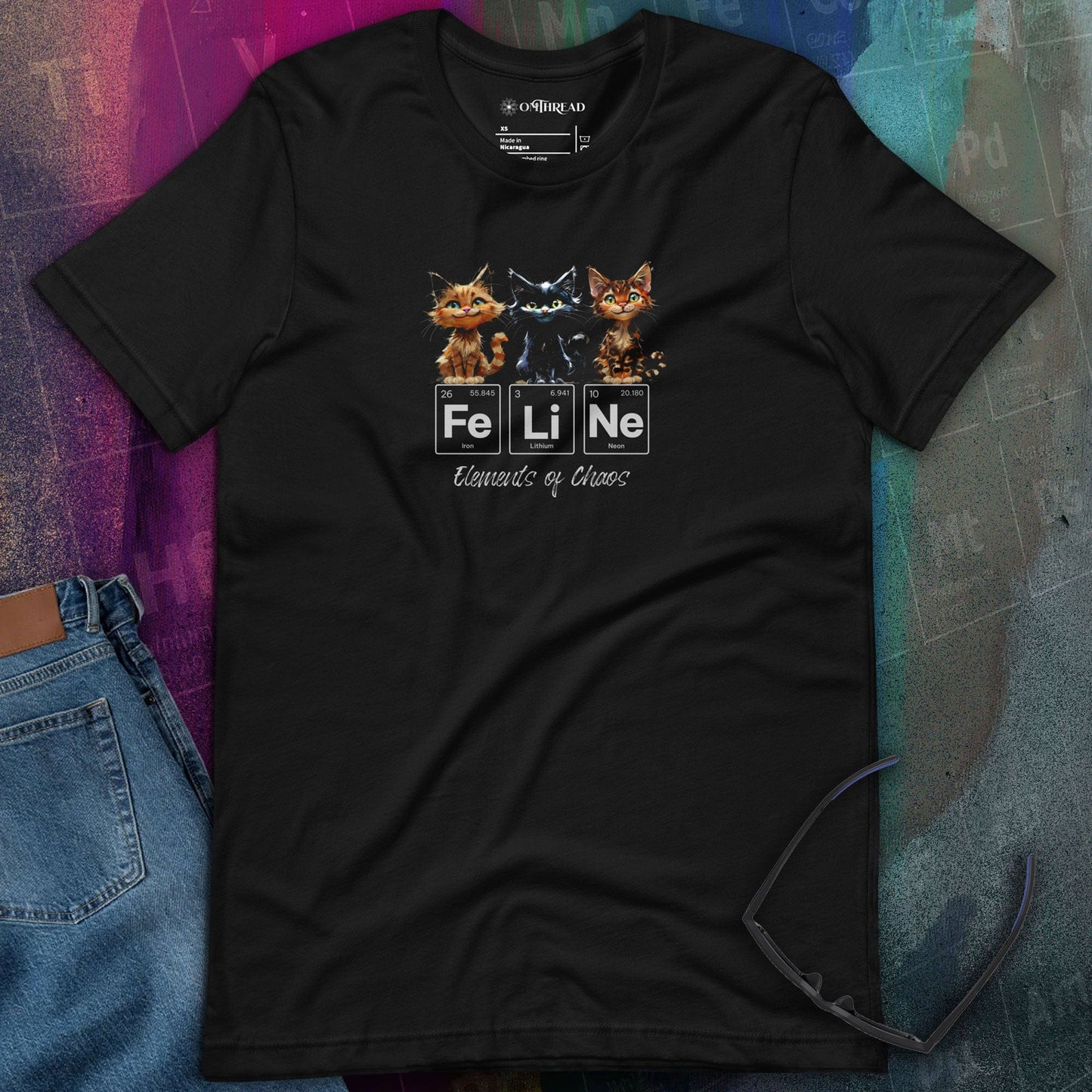OMThread black t-shirt featuring three mischievous cats sitting above the word "FeLiNe," spelled out using periodic table elements Iron (Fe), Lithium (Li), and Neon (Ne). Below, the phrase "Elements of Chaos" is written in cursive font.