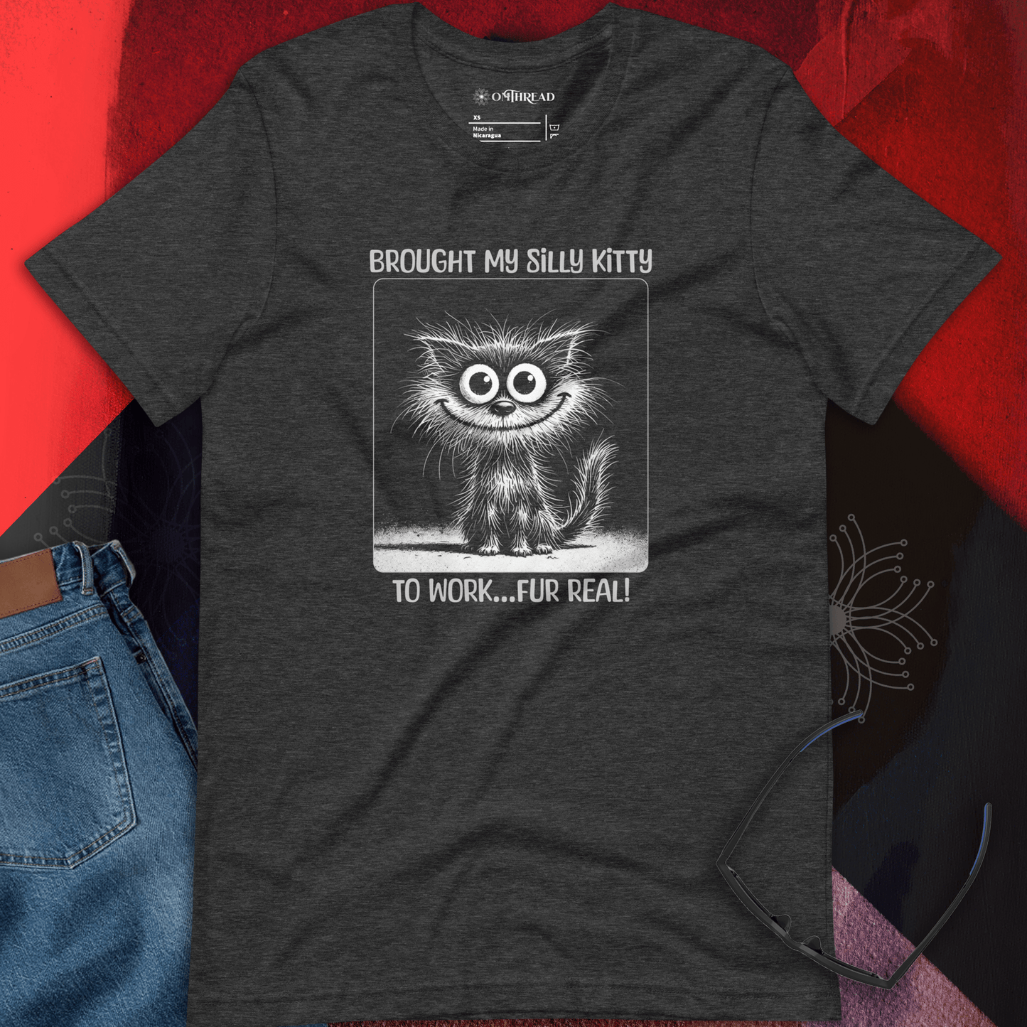 OMThread dark gray t-shirt featuring a hand-drawn, wide-eyed, fluffy cat with a playful expression. The cat is inside a square frame with the phrase "Brought My Silly Kitty to Work... Fur Real!" written in bold, whimsical lettering.