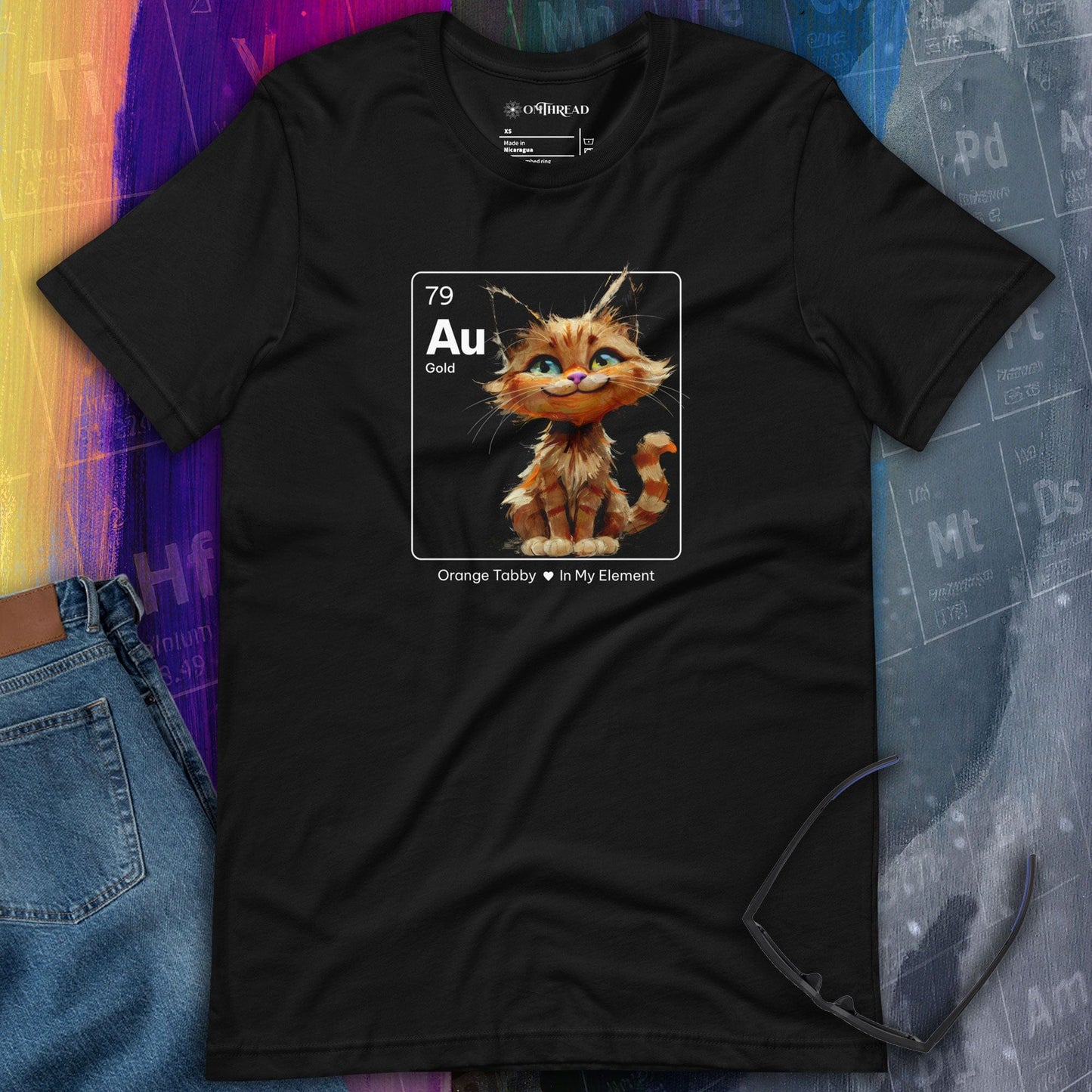 OMThread Gold Element Orange Tabby black t-shirt featuring an orange tabby cat sitting inside a square resembling a periodic table element. The design includes 'Au' for gold, atomic number 79, and the phrase 'Orange Tabby • In My Element.'