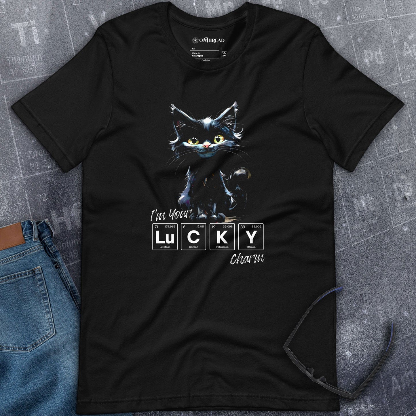 OMThread black t-shirt featuring a whimsical black cat with green eyes standing above the phrase "I'm Your LUCKY Charm," where "LUCKY" is creatively spelled using periodic table elements.