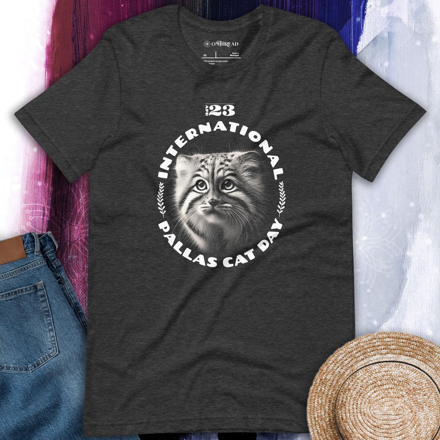 OMThread charcoal gray t-shirt featuring a black-and-white illustration of a Pallas cat kitten inside a circular design with the text "International Pallas Cat Day" and the date "April 23" above.