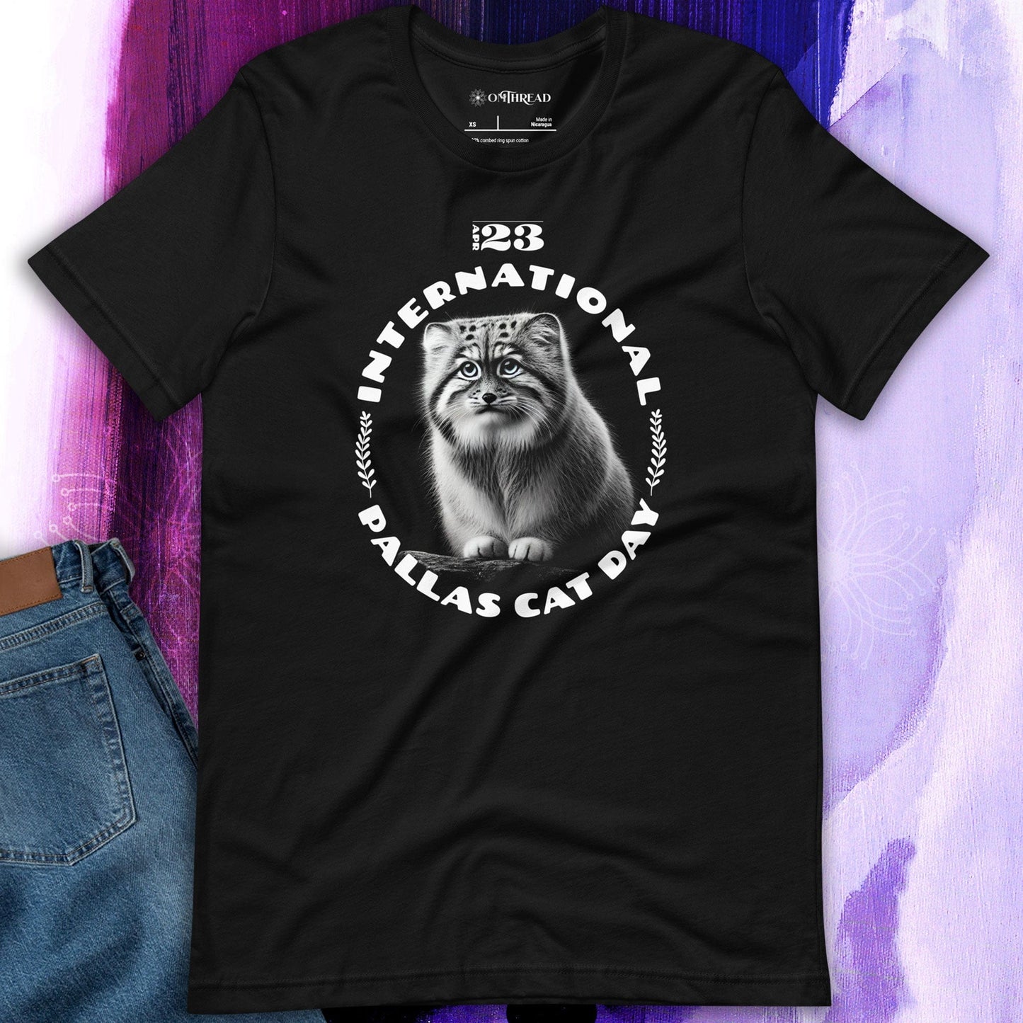 OMThread black t-shirt featuring a detailed black-and-white illustration of a Pallas cat inside a circular design. The words "International Pallas Cat Day" arch around the cat, with "April 23" positioned above.