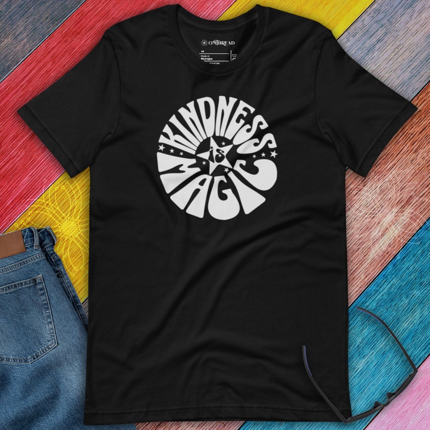 OMTHREAD black t-shirt with white "Kindness is Magic" graphic in retro-style font, featuring a star in the center.