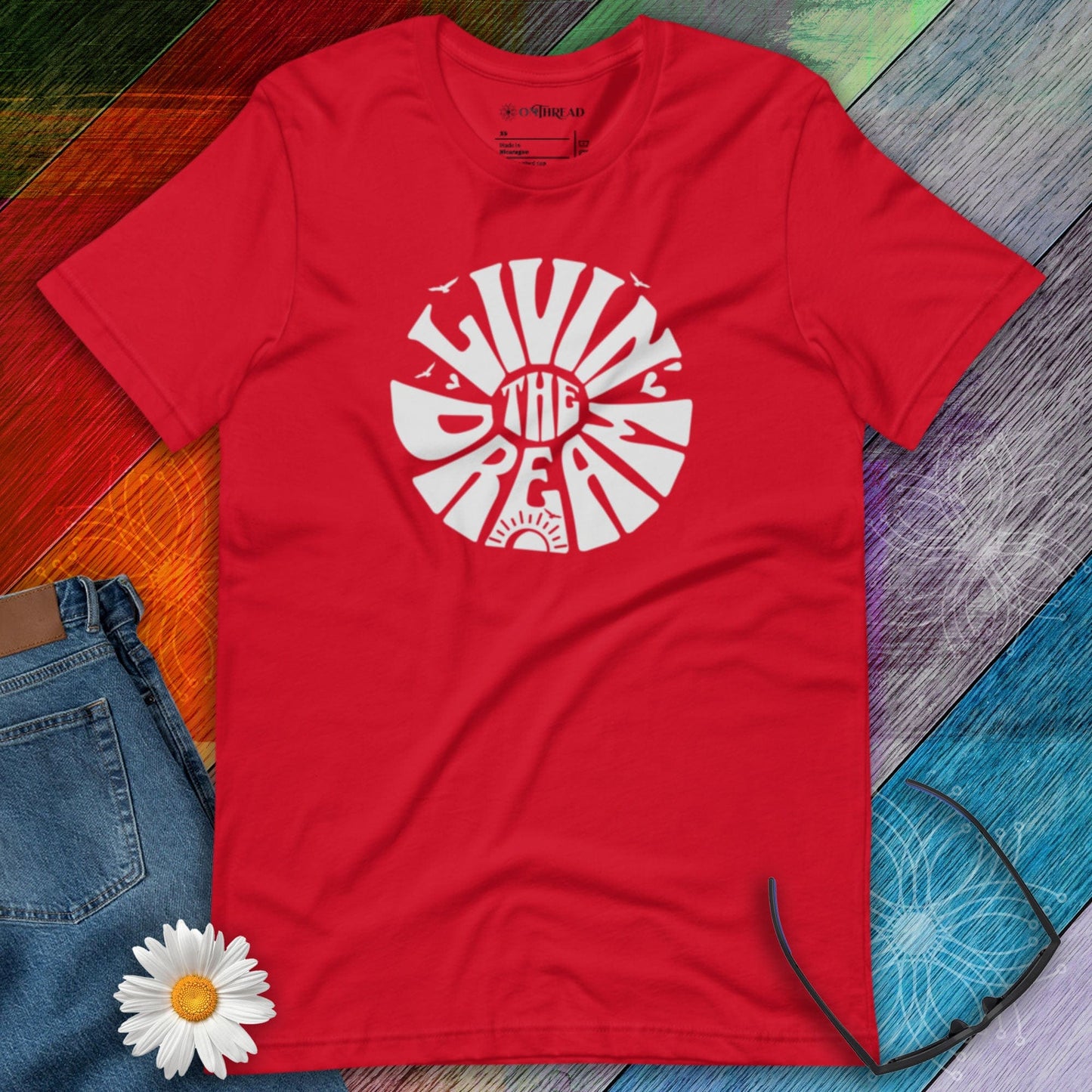 OMTHREAD red t-shirt featuring white retro-style typography reading "Livin' the Dream" in a circular design with sun, birds, and heart elements.