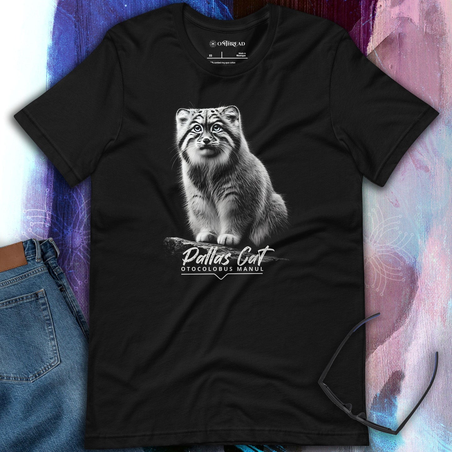 OMThread black t-shirt featuring a detailed black-and-white illustration of a Pallas cat sitting on a branch. The cat has intense eyes and finely detailed fur. Below the image, "Pallas Cat" is written in an elegant script, with "Otocolobus Manul" in a modern font.