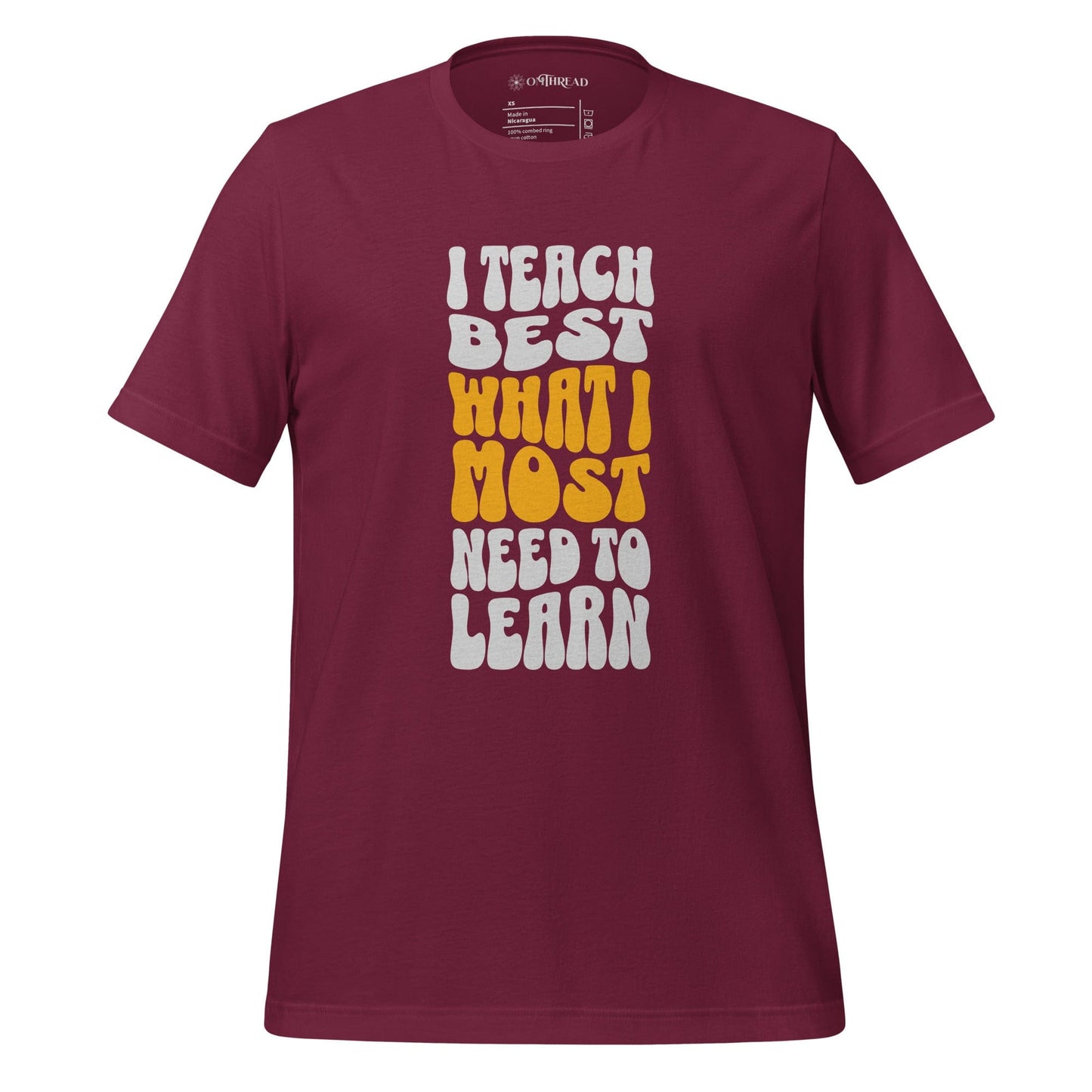 OMTHREAD maroon t-shirt with bold white and yellow text reading "I Teach Best What I Most Need to Learn" in a retro-style font.