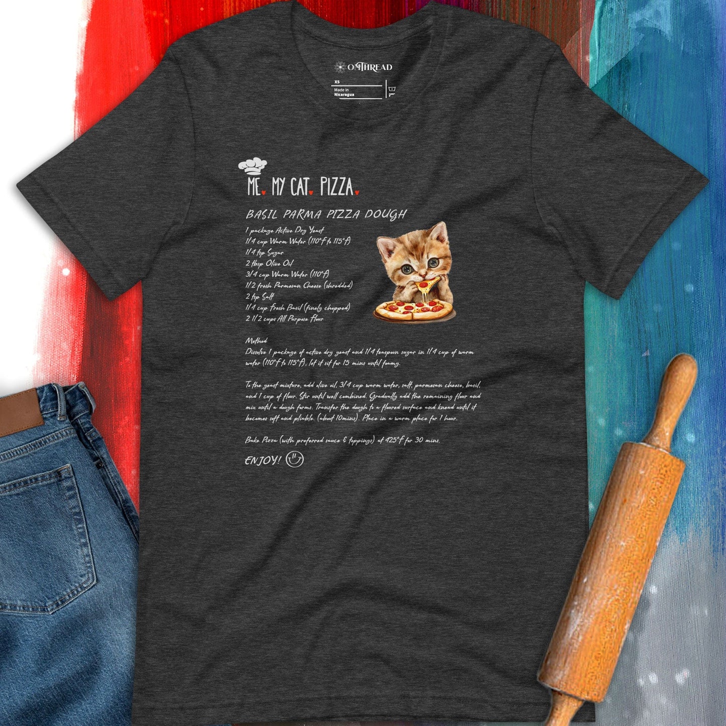 OMThread dark gray t-shirt featuring a playful design of a kitten holding a slice of pizza next to a detailed recipe for basil parmesan pizza dough. The text "Me, My Cat, Pizza" is displayed above the ingredients and instructions, styled in a handwritten font.