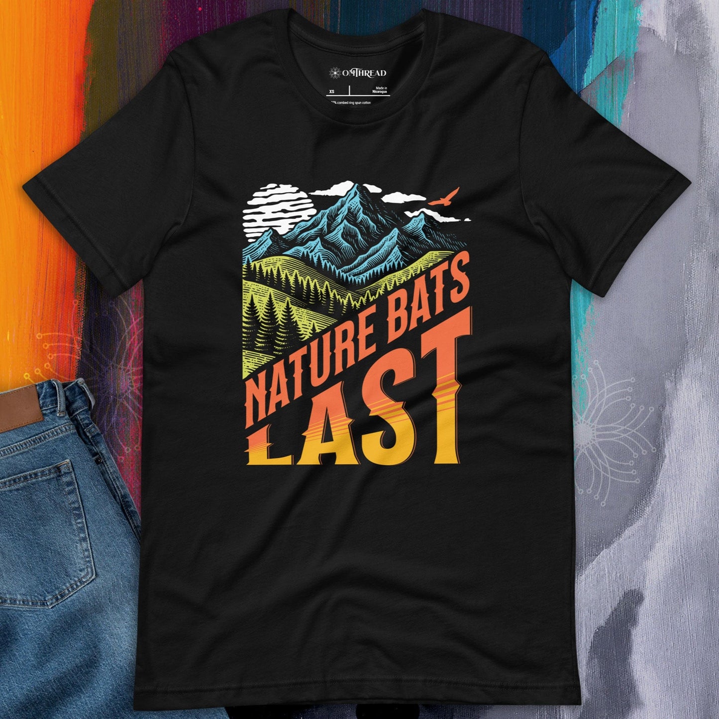 OMThread black t-shirt featuring a bold "Nature Bats Last" design with stylized mountains, forests, and a sunset gradient. High-contrast typography with an outdoor adventure and climate awareness theme.
