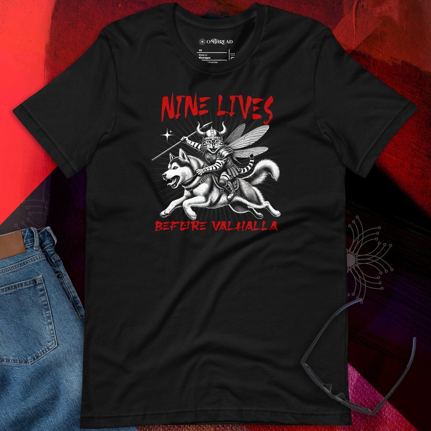 OMTHREAD Nine Lives Before Valhalla Black T-Shirt featuring a Viking cat warrior riding a husky, inspired by Norse mythology. Black tee with bold red text and dynamic artwork.