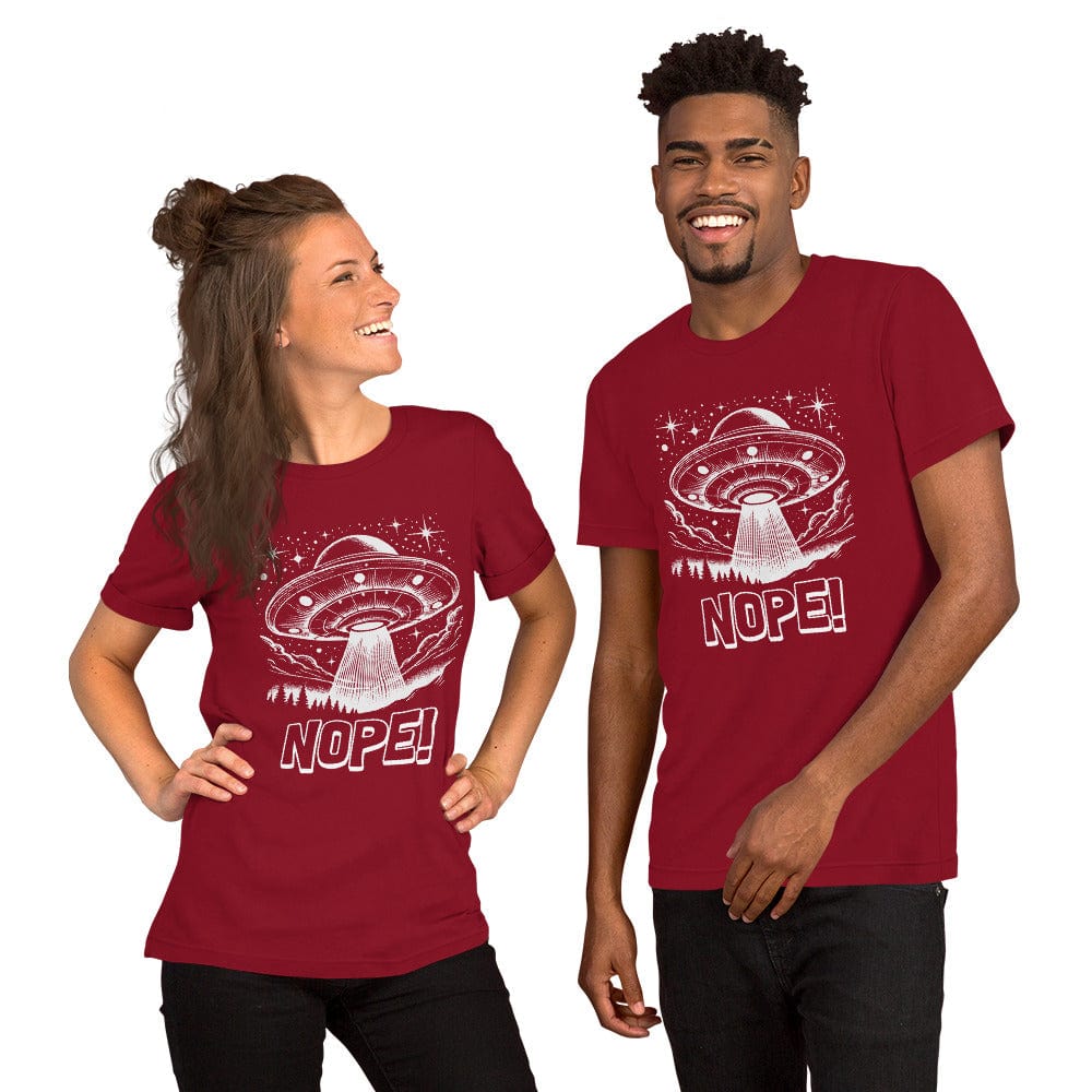 Man and woman wearing crimson red t-shirt featuring a retro-style illustration of a UFO beaming light down onto a forest, surrounded by stars and clouds, with the bold text, NOPE! emphasizing humor and alien themes