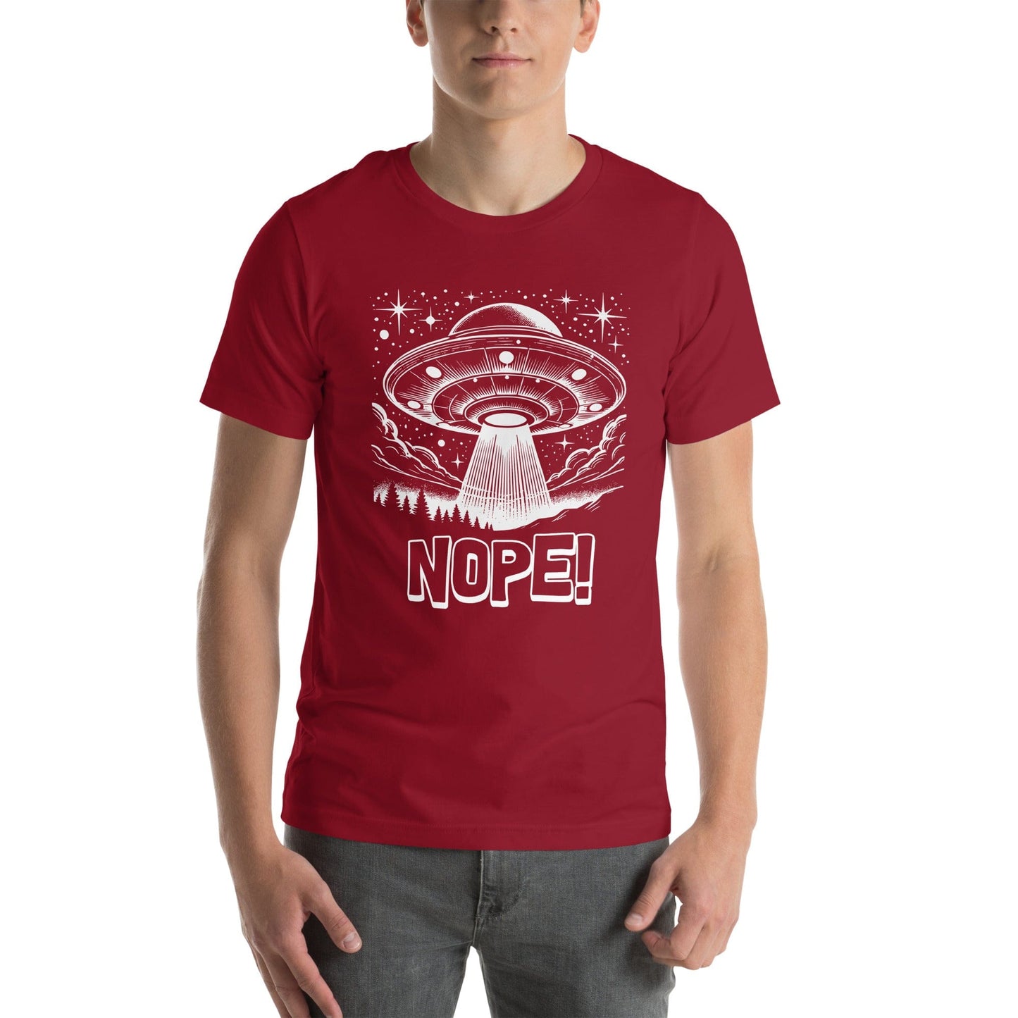 Man wearing crimson red t-shirt featuring a retro-style illustration of a UFO beaming light down onto a forest, surrounded by stars and clouds, with the bold text, NOPE! emphasizing humor and alien themes