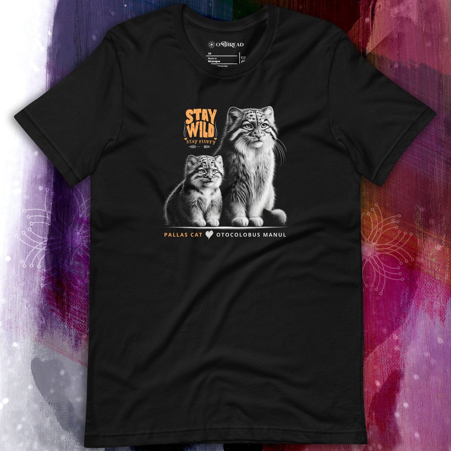 OMThread black t-shirt featuring an illustration of two Pallas cats, one adult and one kitten. The design includes the phrase "STAY WILD STAY FLUFFY" in bold orange text above them and "PALLAS CAT OTOCOLOBUS MANUL" in a clean font below.