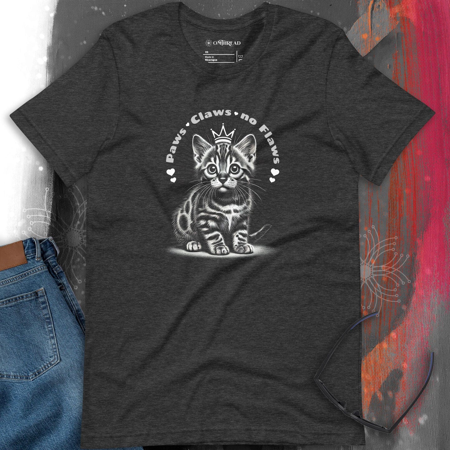 OMTHREAD dark gray t-shirt featuring a detailed illustration of a Bengal kitten wearing a small crown. The phrase "Paws, Claws, no Flaws" arches over the kitten with small decorative hearts.