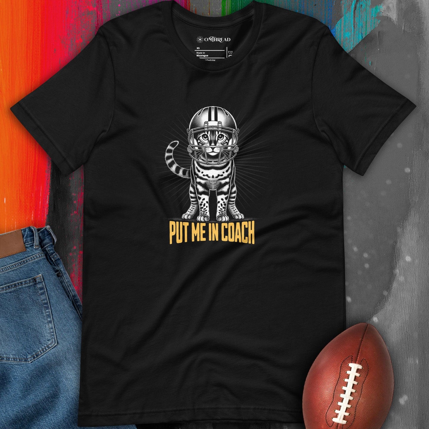 OMTHREAD black t-shirt featuring a Bengal cat in a football helmet with "Put Me In Coach" text. The cat stands with bold linework and a radiant background.