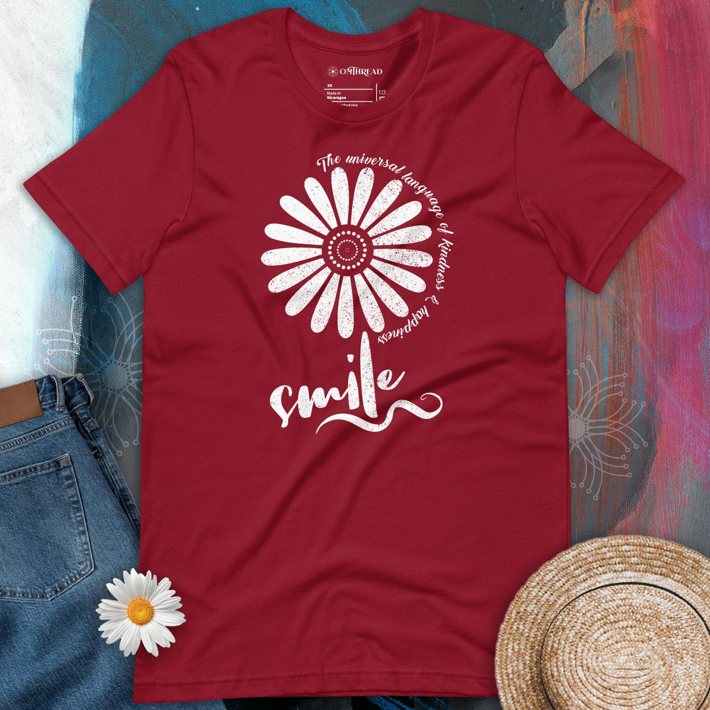OMTHREAD cardinal red t-shirt with a white floral design and the word "smile" in script, surrounded by the phrase "The universal language of kindness & happiness" in a circular pattern