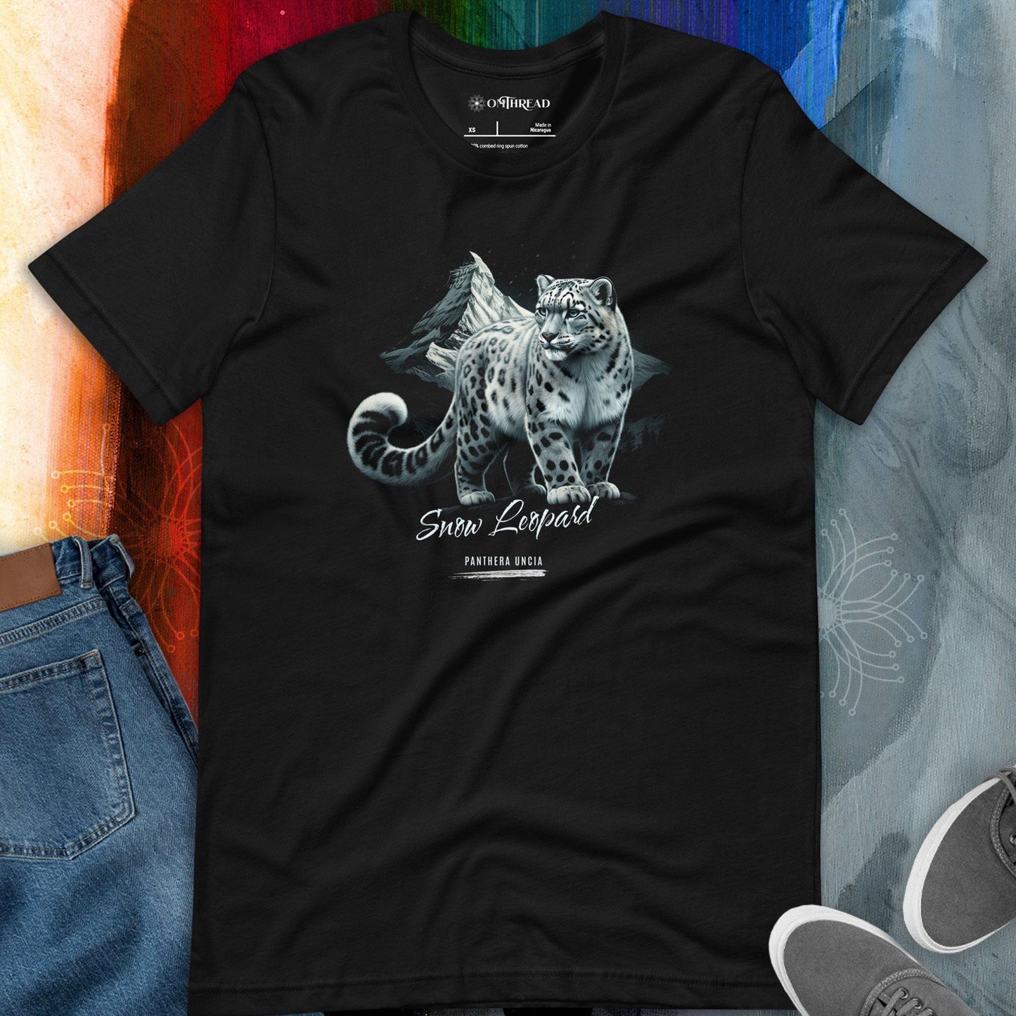 OMThread black t-shirt featuring a detailed illustration of a snow leopard standing on a rocky ledge with a mountain landscape in the background. The design includes the text "Snow Leopard" and "Panthera Uncia" in elegant typography.