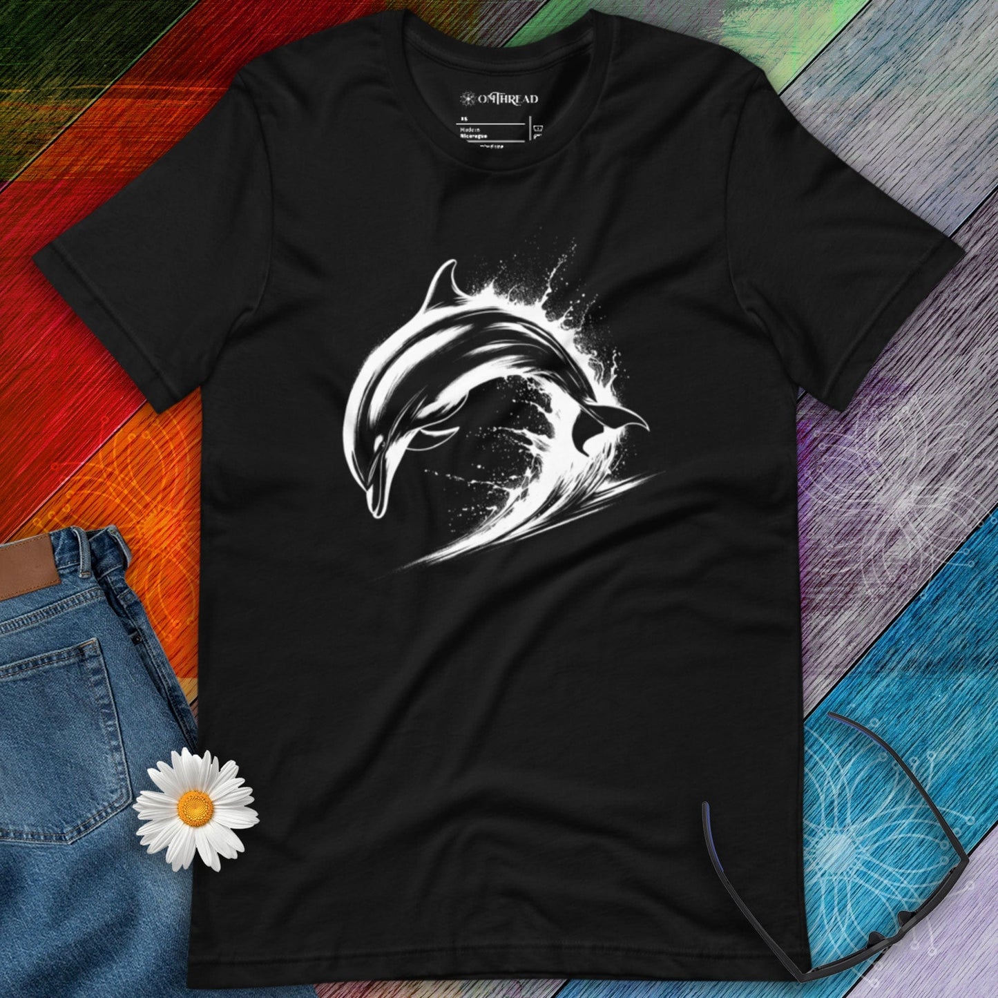 OMTHREAD black t-shirt featuring a white dolphin mid-leap over ocean waves, designed in a bold, high-contrast style.