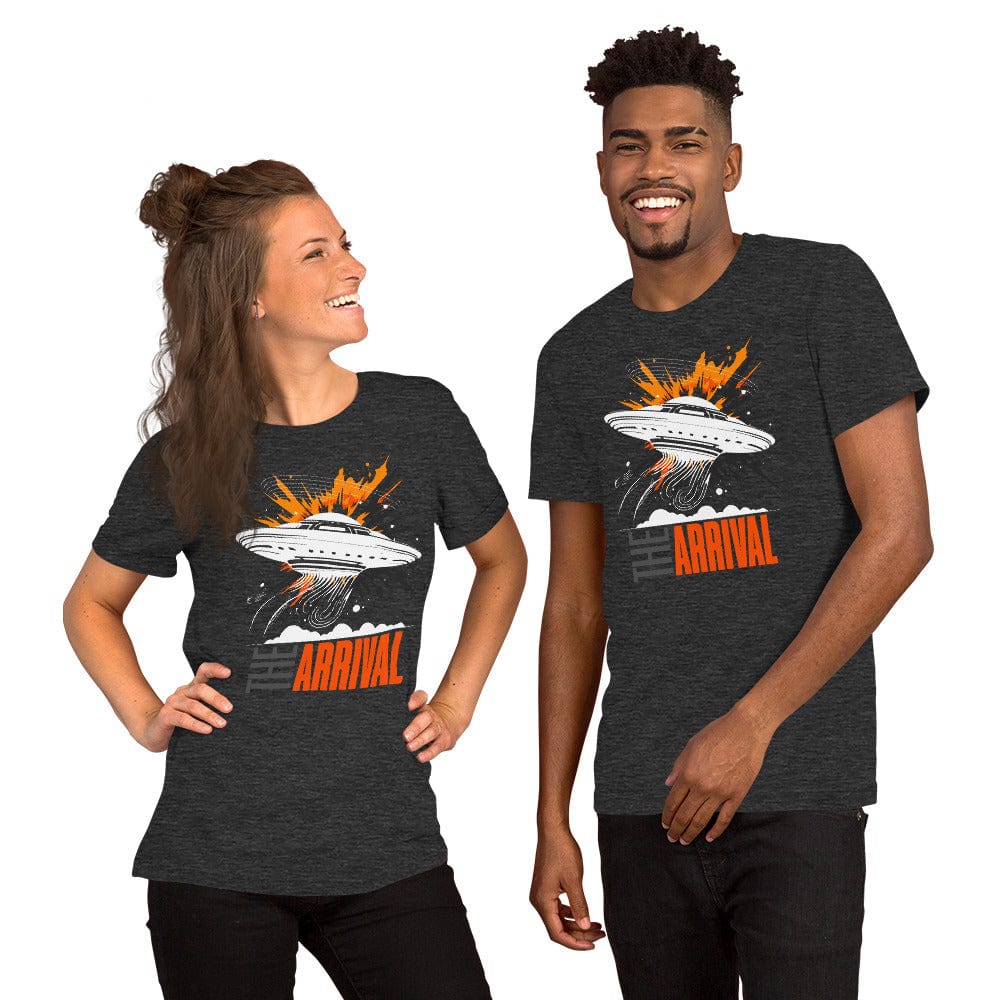Man and woman wearing dark gray t-shirt showcasing a bold design of a UFO emitting glowing beams, surrounded by explosive orange accents, clouds, and dynamic motion lines, with the text, THE ARRIVAL in contrasting gray and orange, blending sci-fi and graphic art.