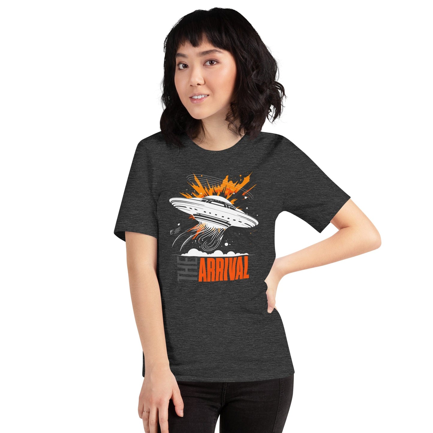 Woman wearing dark gray t-shirt showcasing a bold design of a UFO emitting glowing beams, surrounded by explosive orange accents, clouds, and dynamic motion lines, with the text, THE ARRIVAL in contrasting gray and orange, blending sci-fi and graphic art.