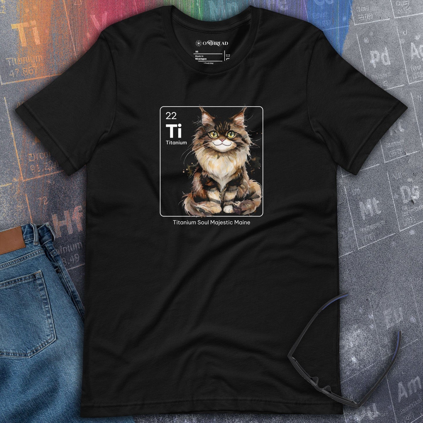 OMThread black t-shirt featuring a Maine Coon cat illustration within a periodic table-inspired square labeled "Ti" for Titanium. The text below reads "Titanium Soul Majestic Maine." The design combines chemistry elements with feline charm.