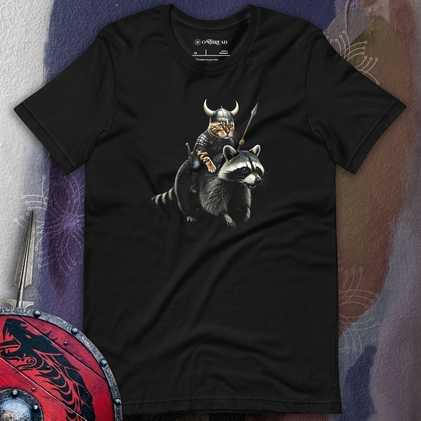 OMThread Viking Cat Warrior black t-shirt featuring a detailed black and white illustration of a Viking cat wearing a horned helmet and armor, holding a spear, and riding a fierce-looking raccoon.