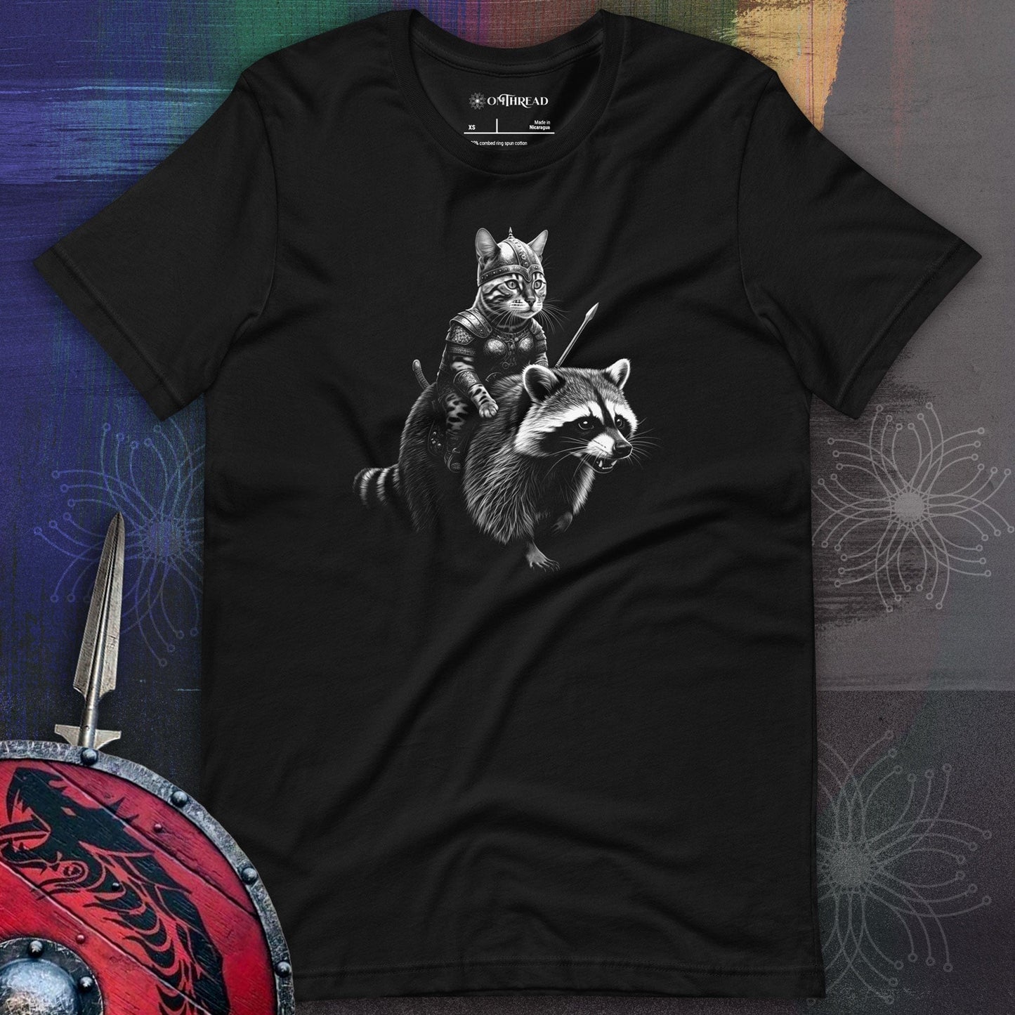 OMThread black t-shirt featuring a Bengal cat dressed as a Viking warrior, wearing a horned helmet and armor while holding a spear. The cat is riding a detailed illustration of a strong raccoon.