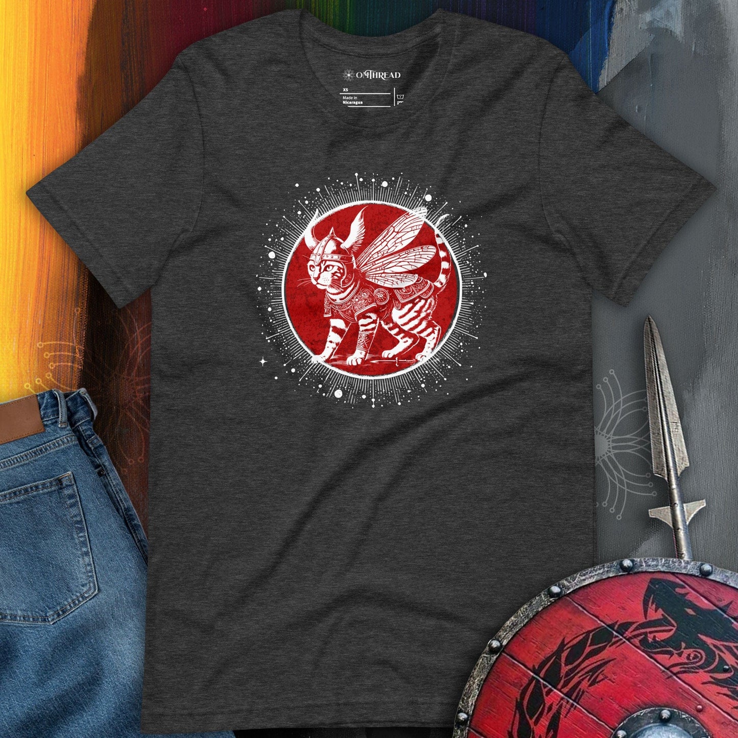 OMThread dark gray t-shirt featuring a Viking cat with wings, wearing Norse-inspired armor, set against a red circular backdrop with celestial details. The feline has intricate markings and an intense gaze.