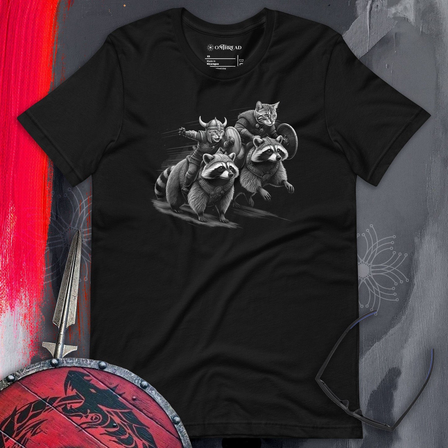 OMTHREAD black t-shirt featuring two Viking cats in armor and helmets, riding armored raccoons. One cat holds a sword, the other carries a shield. The design is intricately detailed, depicting dynamic motion and a fantasy warrior theme.