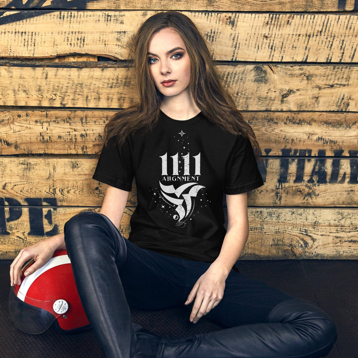 Woman model wearing a black t-shirt with a white graphic design featuring the number 1111 above the word 'Alignment' and an abstract bird-like symbol surrounded by stars and cosmic elements.