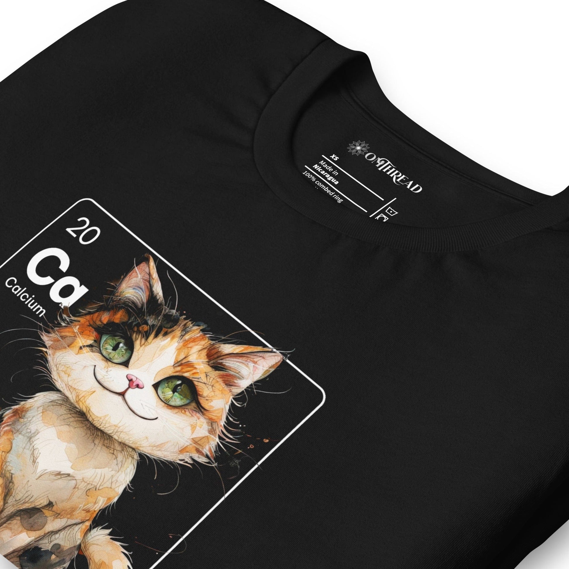 Black t-shirt featuring a periodic table-inspired design of a charming, illustrated calico cat within a square labeled 'Ca' for Calcium. Text below reads 'Cal-lico Charm