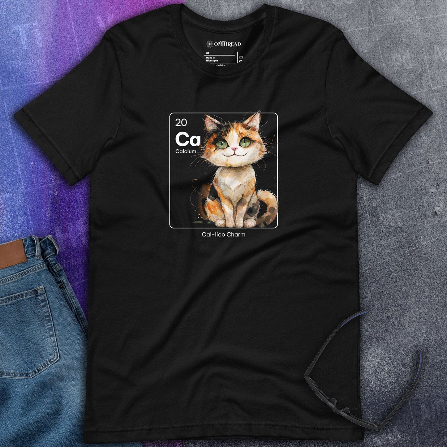 Black t-shirt featuring a periodic table-inspired design of a charming, illustrated calico cat within a square labeled 'Ca' for Calcium. Text below reads 'Cal-lico Charm