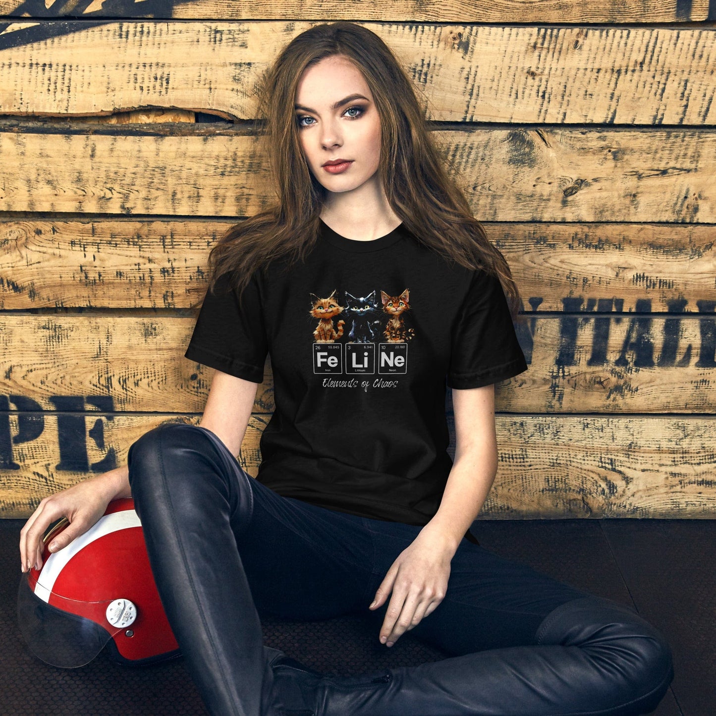 Female model wearing a black t-shirt featuring three mischievous kittens sitting above the word 'FeLiNe,' spelled out using periodic table elements: Iron (Fe), Lithium (Li), and Neon (Ne). Below, the phrase 'Elements of Chaos' is written in cursive font.