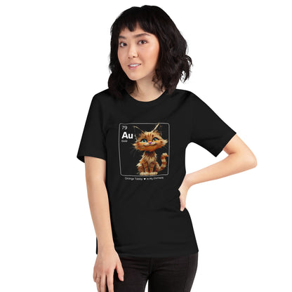 Woman wearing a black t-shirt featuring an orange tabby cat sitting cheerfully inside a square design resembling a periodic table element. The square includes 'Au' for gold, the atomic number 79, and the text 'Orange Tabby In My Element' underneath.