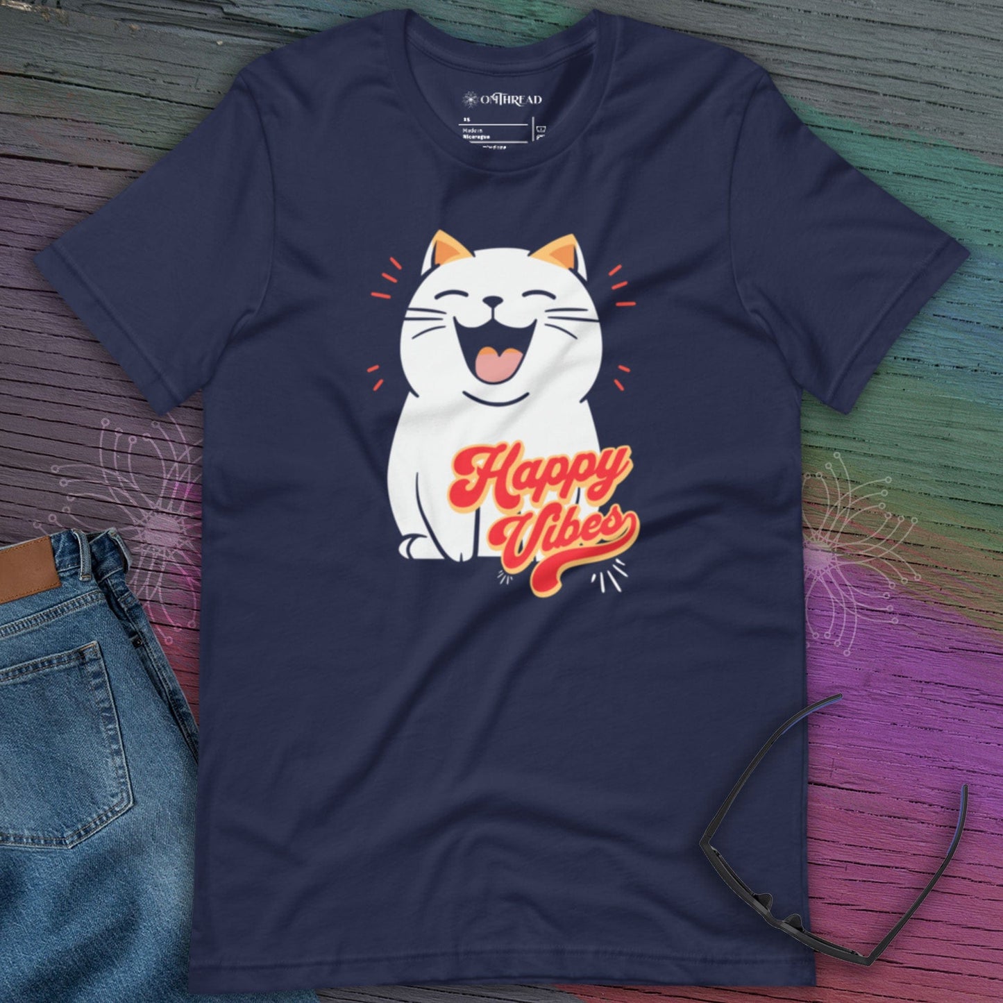 Navy blue t-shirt featuring a cheerful white cartoon cat with closed eyes and a big smile. The cat is surrounded by red lines for emphasis, and the phrase 'Happy Vibes' is written in bold, retro-style orange and yellow lettering below it.