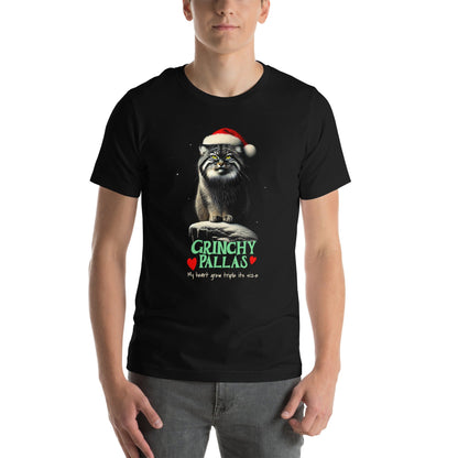 Man wearing black t-shirt featuring a Pallas cat wearing a Santa hat, sitting on a snowy rock with a grumpy expression. The text below reads 'GRINCHY PALLAS' in green and red, with the phrase 'My heart grew triple its size' underneath.