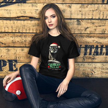 Woman wearing black t-shirt featuring a Pallas cat wearing a Santa hat, sitting on a snowy rock with a grumpy expression. The text below reads 'GRINCHY PALLAS' in green and red, with the phrase 'My heart grew triple its size' underneath.