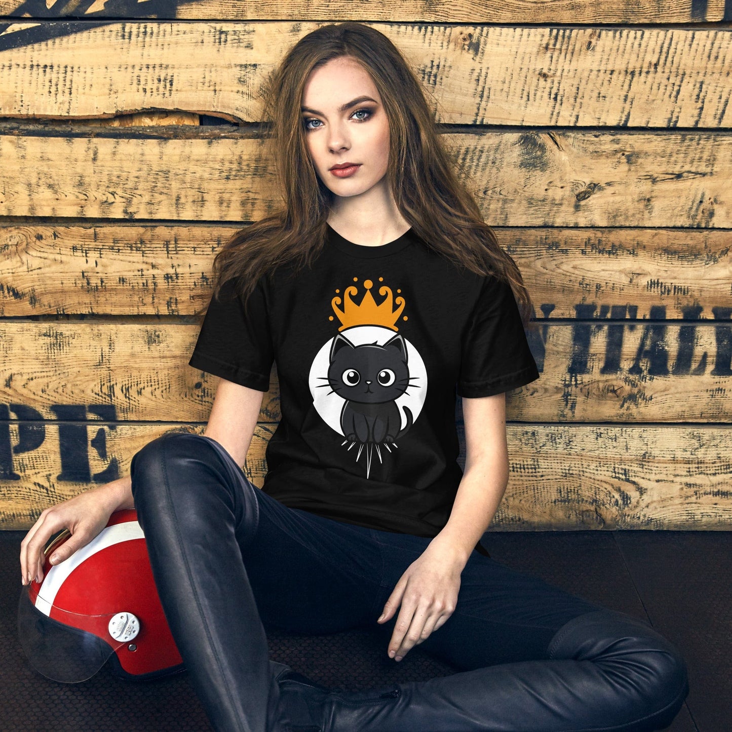 Female model wearing an OMThread black t-shirt featuring a cute black cat with a golden crown, posed against a rustic wooden background, blending fashion with feline charm.