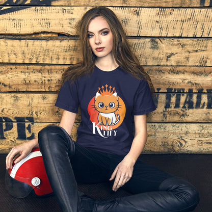 A woman wearing the navy "King Kitty" t-shirt in a casual, laid-back setting with a wooden backdrop. The vibrant cat design and the bold lettering contrast beautifully with the navy background, making it an eye-catching piece for cat enthusiasts. 