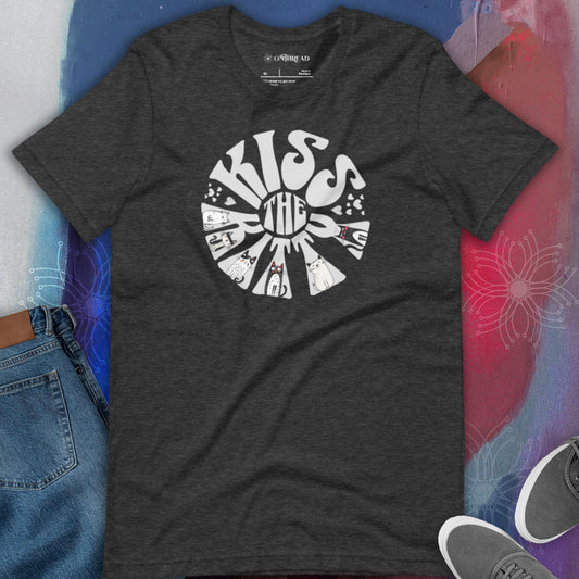 Dark gray t-shirt with a circular, retro-style design that reads 'Kiss the Kitty.' The letters form a sunburst shape with playful illustrations of various cats integrated into the text and surrounding shapes.