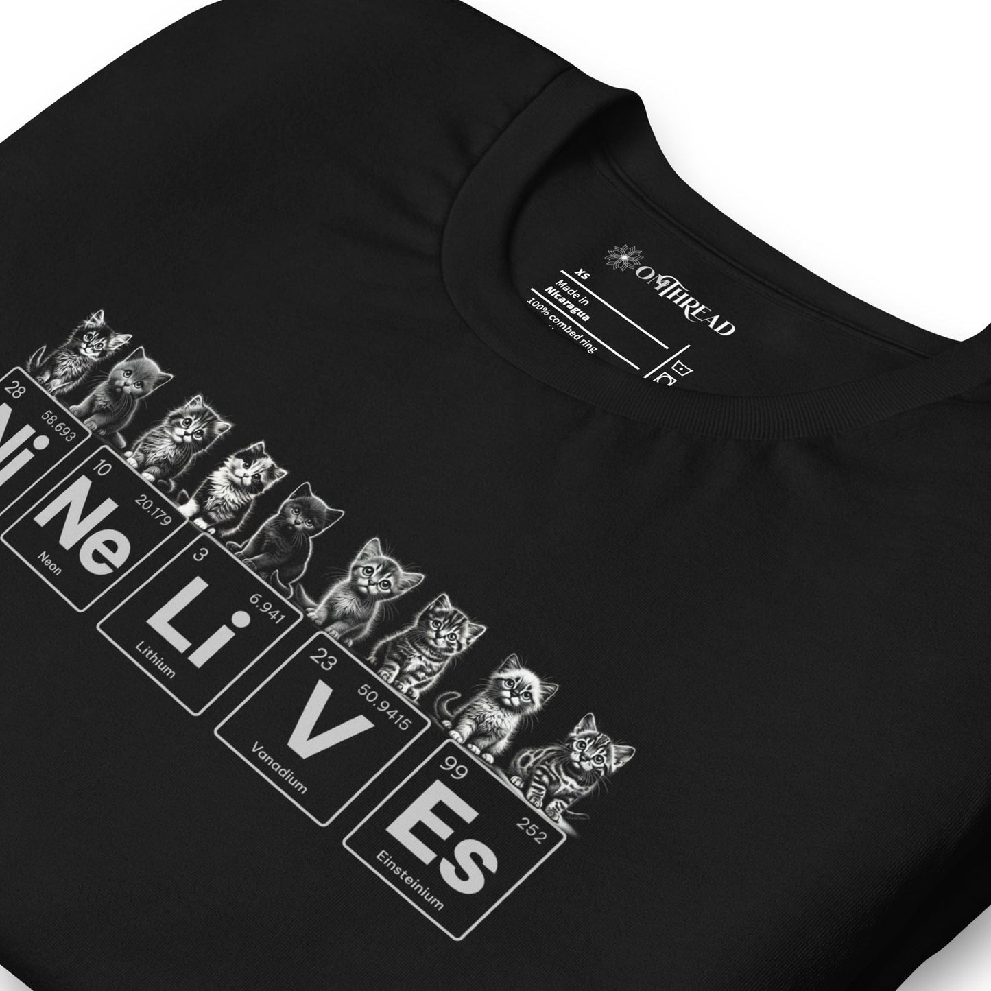 A black t-shirt featuring nine illustrated kittens, each with playful expressions, sitting above periodic table elements that spell 'Ni Ne Li V Es' (Nickel, Neon, Lithium, Vanadium, and Einsteinium), representing 'Nine Lives.