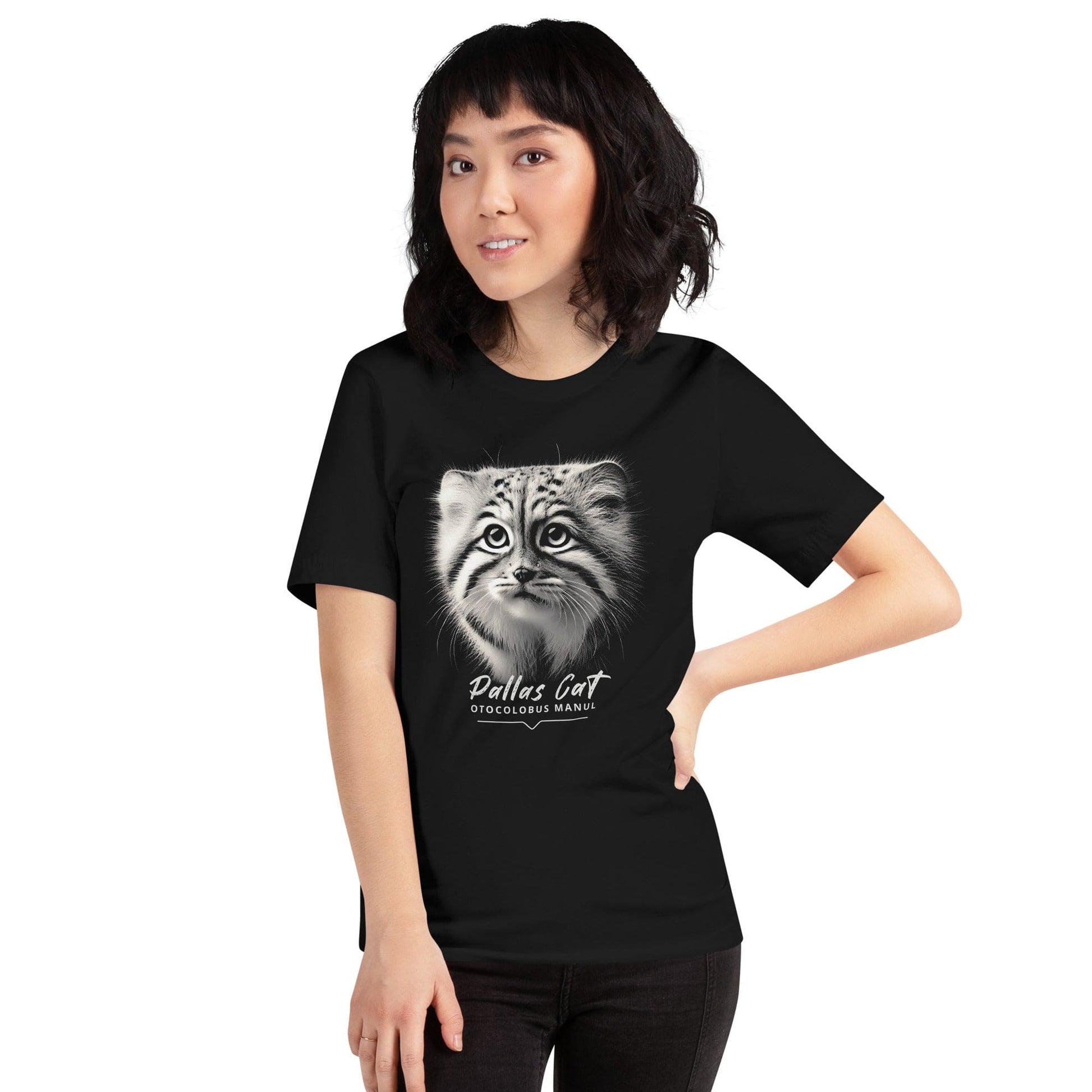 Woman wearing black t-shirt featuring a close-up, black-and-white illustration of a Pallas kitten's face with striking fur details and intense eyes. Below the image, 'Pallas Cat' is written in elegant white script, followed by 'Otocolobus Manul' in smaller capital letters.