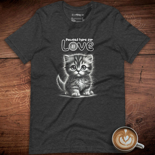 OMThread dark gray t-shirt featuring a black and white illustration of a fluffy kitten with large expressive eyes. Above the kitten, the phrase "Pawsed Here for Love" is written in a playful font, with the word "Love" incorporating a pause button symbol.