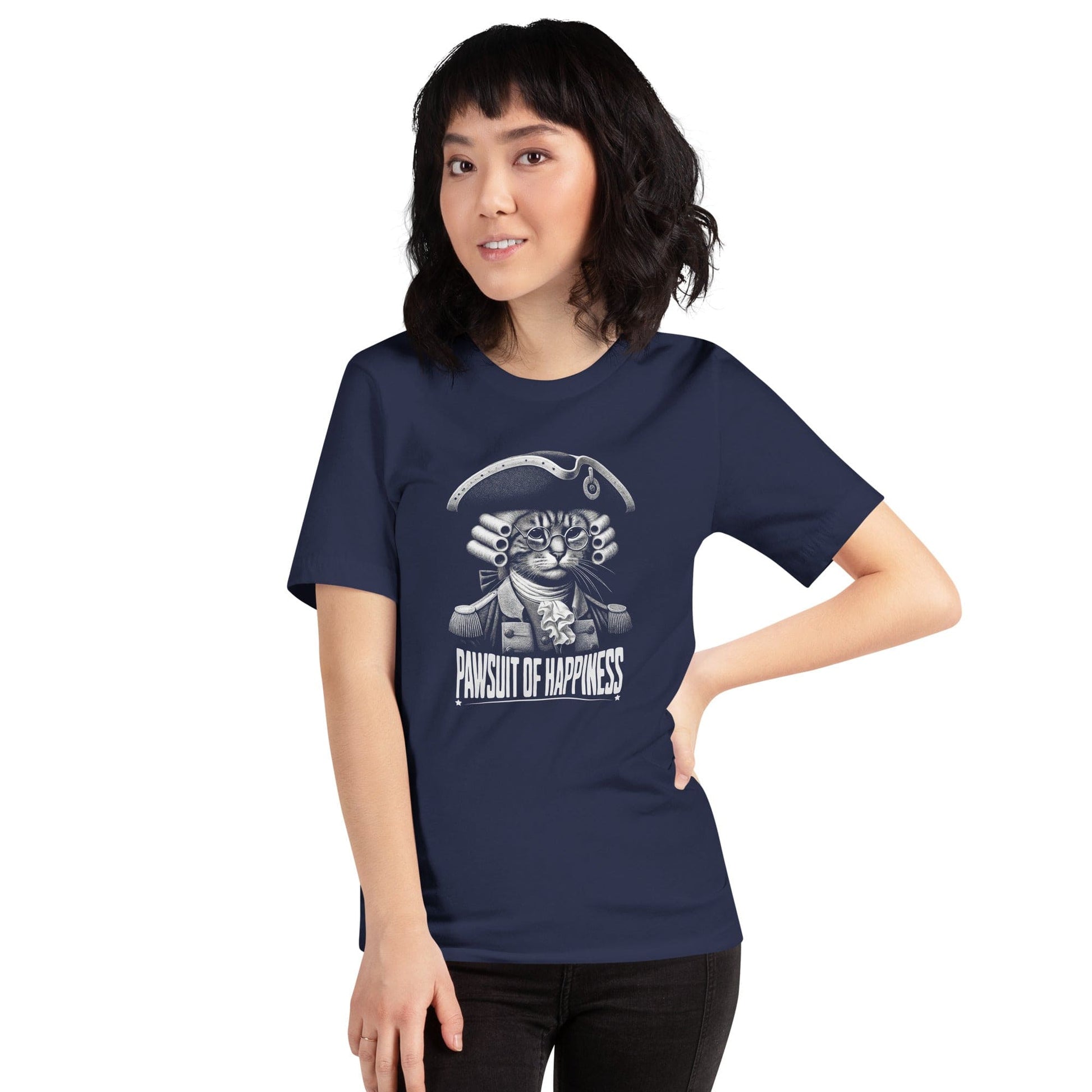 Woman wearing navy blue t-shirt featuring a humorous design of a cat dressed as a founding father in colonial attire, complete with a tricorne hat and glasses. The text, Pawsuit of Happiness is displayed below in bold, styled with stars and a decorative arch.