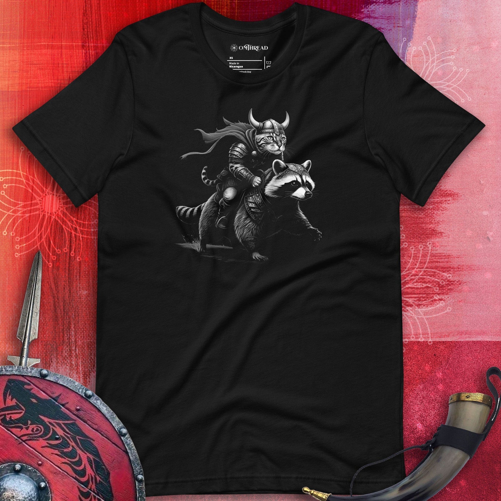 Black t-shirt featuring a Viking-themed illustration of a warrior cat wearing a horned helmet and armor, riding a fierce armored raccoon. The background includes Viking-themed elements like a shield and horn.