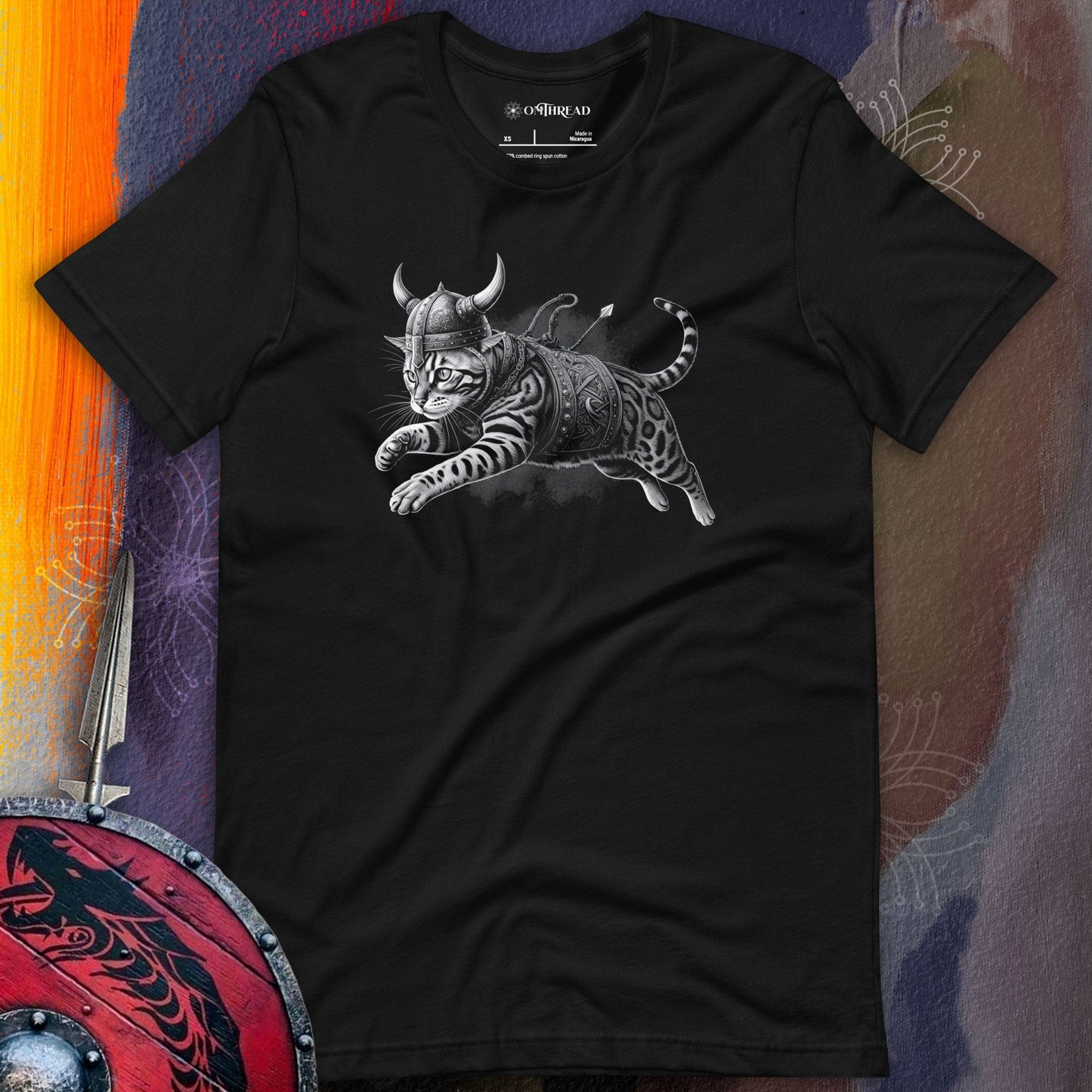 Black t-shirt featuring an illustration of a fierce cat dressed as a Viking warrior, complete with a horned helmet, armor, and weapons, leaping into action. The background includes a Viking shield and sword.