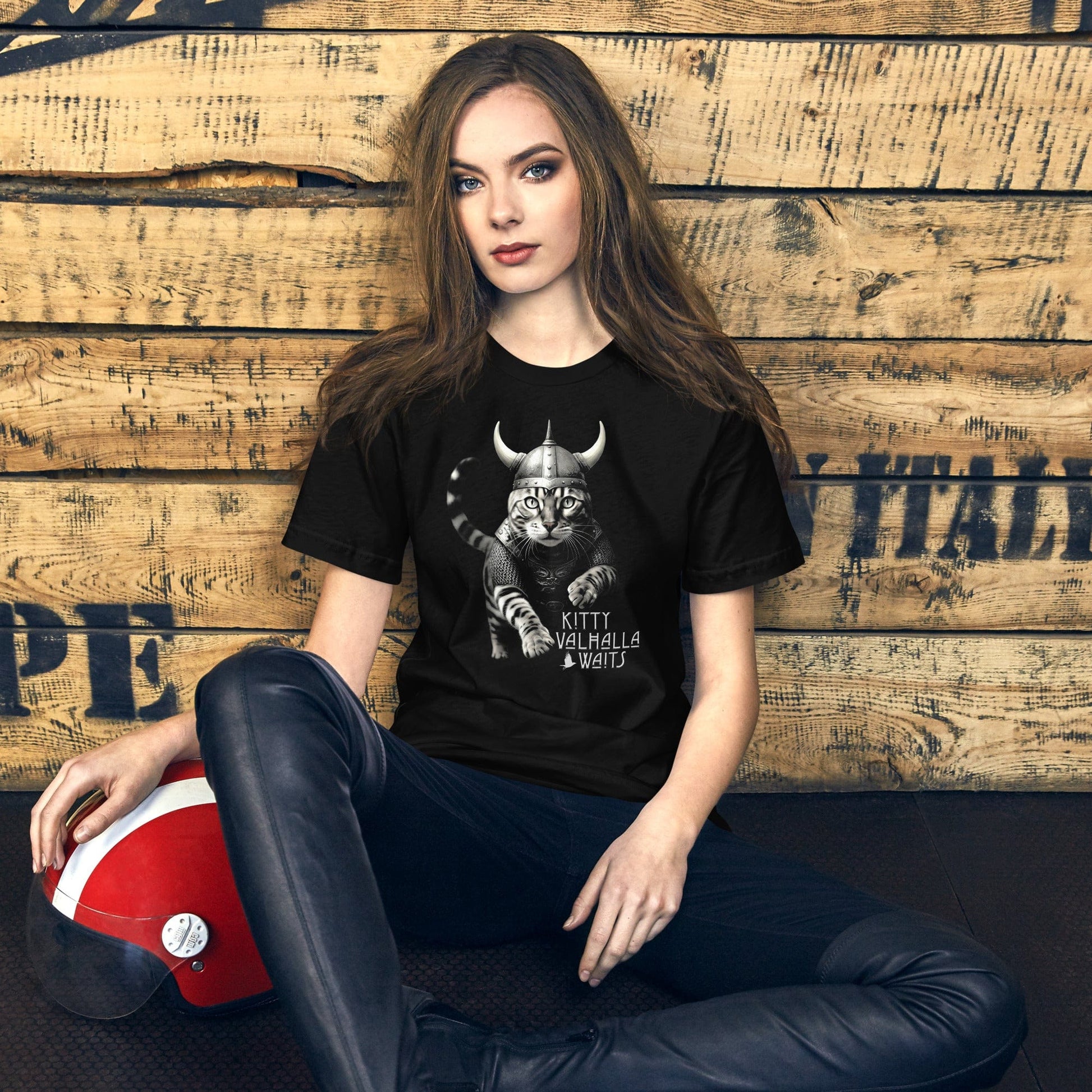 A female model wearing a black t-shirt featuring a Viking-themed design of a fierce bengal cat wearing a horned helmet and armor. The text below reads 'Kitty Valhalla Waits' in bold, stylized font. 